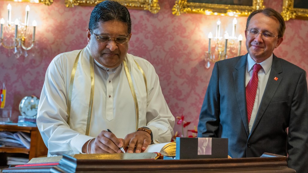 Der Sri  Lankische Botschafter steht im Bürgermeisteerzimmer. vor einem Stehpult und trägt sich in das Goldene Buch ein. Rechts hinter ihm im Bild, ist Bürgermeister Matthias Stadler zu sehen.