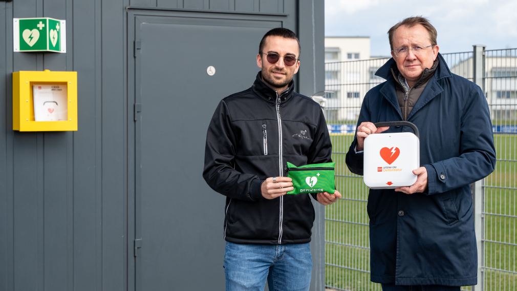 Sportbeauftragter Florian Gleiss und Bürgermeister Matthias Stadler mit dem neuen Defibrillator auf der Stadtsportanlage. (Foto: Christian Krückel)