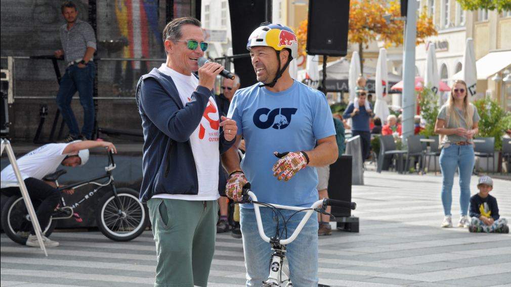 Ein Foto der BMX-Stunt-Show am Rathausplatz mit Publikum und den Infoständen der diversen Aussteller:innen. (Foto: Wolfgang Mayer)