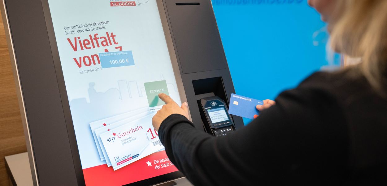 Eine Frau steht am St. Pöltner Rathausplatz und hält einen Fächer aus St. Pölten Gutscheinen vor sich. Foto: Tanja Wagner