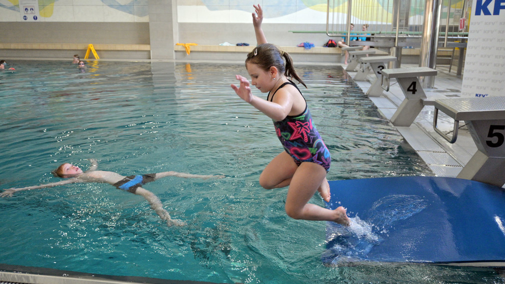 Ein Mädchen, das an einem Selbstrettungsschwimmtraining teilnimmt, springt in ein Schwimmbecken.