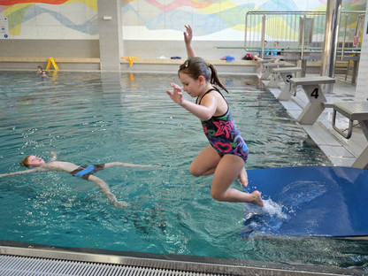 Ein Mädchen, das an einem Selbstrettungsschwimmtraining teilnimmt, springt in ein Schwimmbecken.