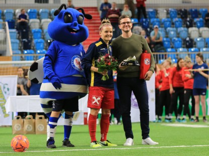 SKN Spielerin Isabelle Meyer bei Blumenübergabe mit Fußball Maskotchen auf Spielfeld