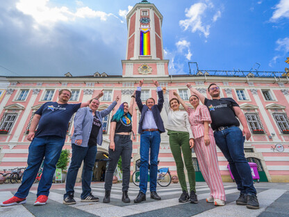 ST. Pride Vereinsmitglieder Erwin Rossmann, Elke Bandion, Tris Endl, Bürgermeister Matthias Stadler, Ilse Knell und Mariella Schlossnagl vom Büro für Diversität und ST. Pride Vereinsobmensch Oskar Beneder vor dem Rathaus mit Progress Pride Fahne am Rathausturm. (Foto: Arman Kalteis)