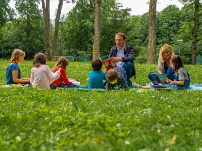 Kindern wird im Park vorgelesen von zwei Erwachsenen. (Foto: Arman Behpournia)