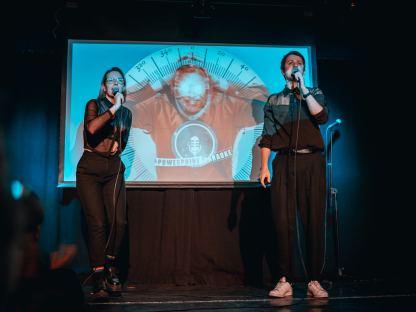 Zwei Personen stehen vor einer Powerpoint Präsentation auf einer Bühne. Foto: Petra Weixelbraun