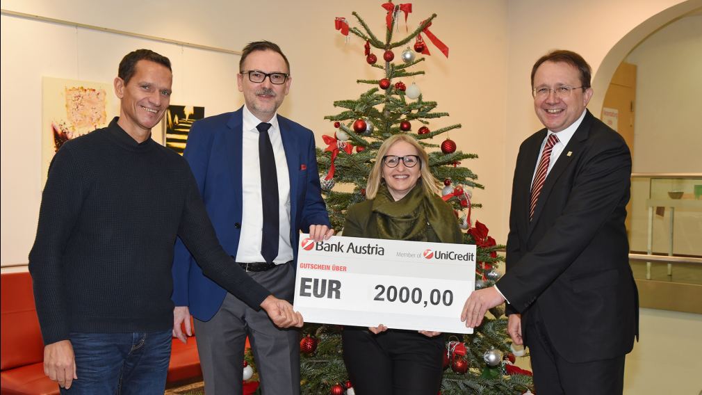 Vier Personen posieren mit dem gespendeten Gutschein der Bank Austria vor einem Weihnachtsbaum im Rathaus. (Foto: Josef Vorlaufer)