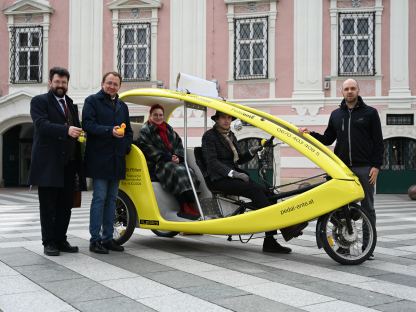 Eine gelbe Fahrrad-Rikscha mit Menschen die drinnen sitzen und rundherum stehen. (Foto: Arman Kalteis)
