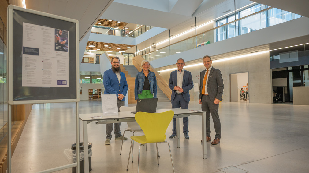 Vier Personen befinden sich im neuen Gebäude der Fachhochschule St. Pölten und lachen für ein Gruppenfoto in die Kamera.