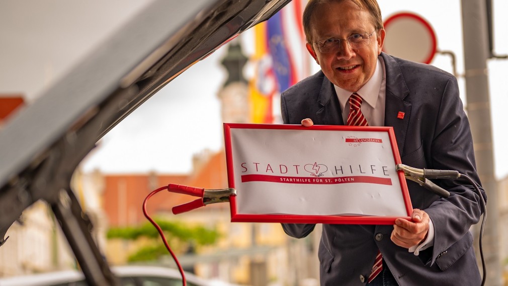 Bürgermeister Matthias Stadler mit "Stadthilfe"-Schild vor einem Auto am Rathausplatz. (Foto: Arman Kalteis)