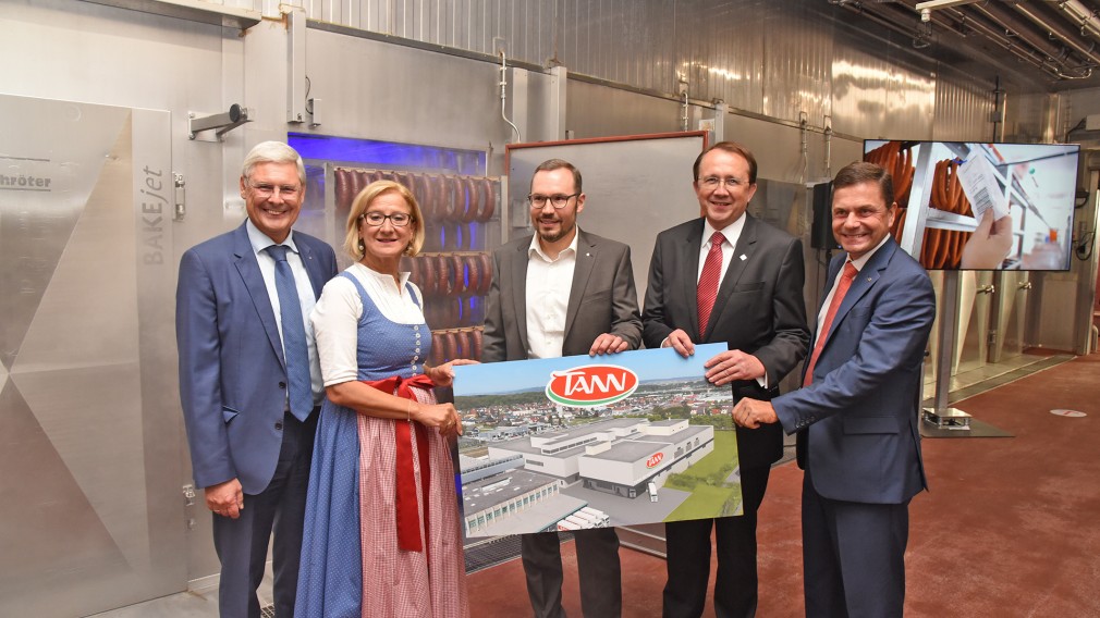 Vier Männer und eine Frau halten ein Schild in der Hand und positionieren sich für ein Gruppenfoto.