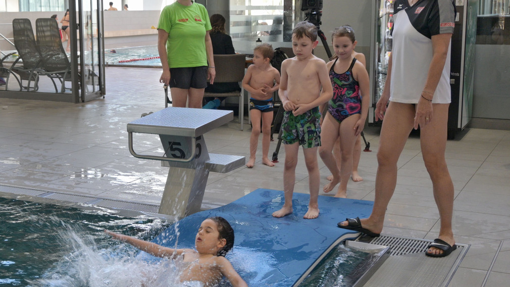 Ein Mädchen, das an einem Selbstrettungsschwimmtraining teilnimmt, springt in ein Schwimmbecken.