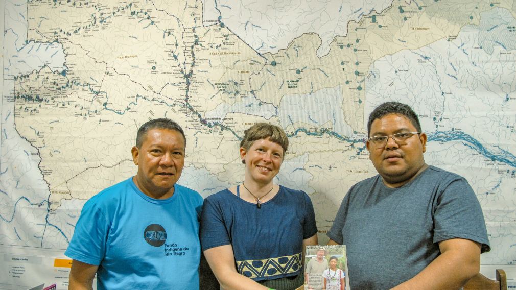 Rio Negro-Koordinatorin Kerstin Plaß mit den Partnern der FOIRN vor einer Karte des geschützten Gebiets. In ihren Händen halten sie ein Bild von Klimabündnis-Mitarbeiter Johann Kandler, welcher die Partnerschaft in den 1990ern aufbaute. (Foto: Klimabündnis Österreich 