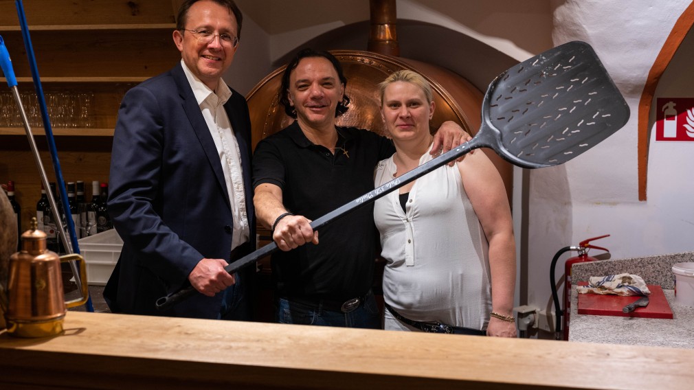 Bürgermeister Mag. Matthias Stadler gratuliert Michele Madonna und seiner Frau zur Eröffnung. Im Bild sind alle drei mit einem großen Pizzaheber zu sehen (Foto: Arman Behpournia).