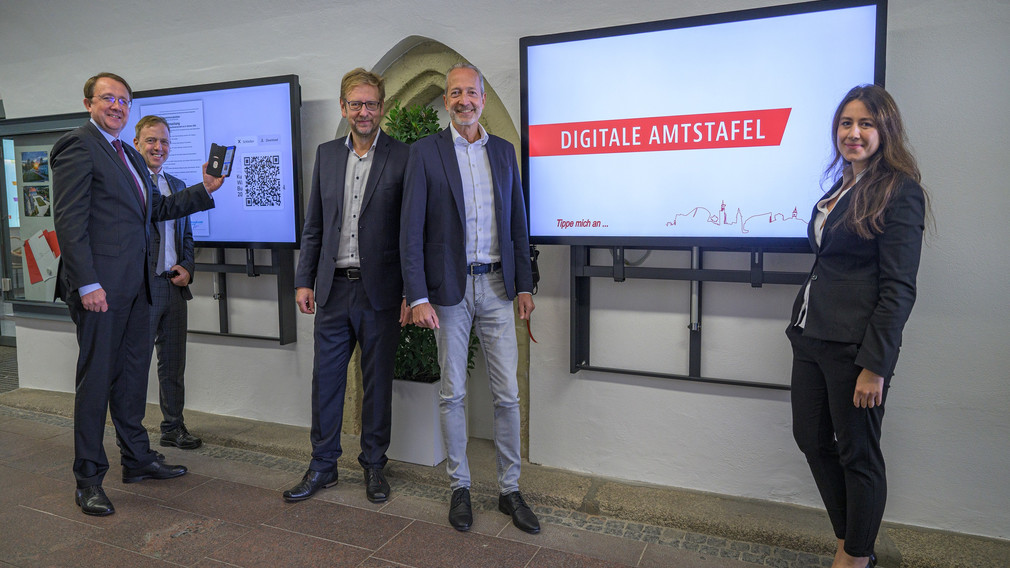 Fünf Personen vor der neuen, digitalten Amtstafel im Rathaus-Eingang. (Foto: Kalteis)