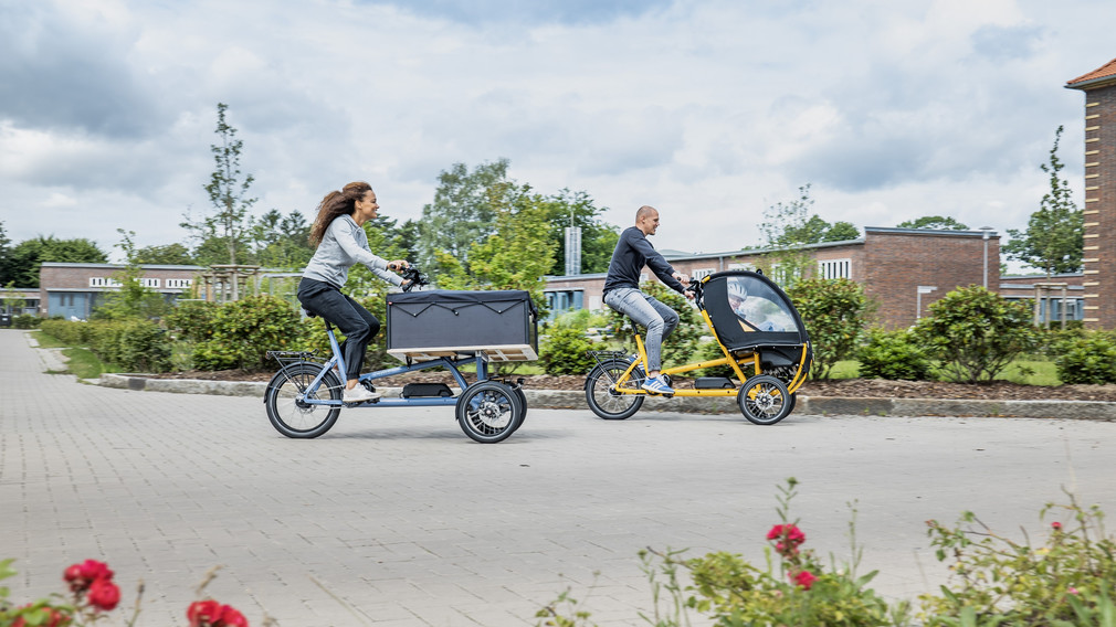 Vater, Mutter und Kind fahren mit einem Lastenrad durch die Stadt.
