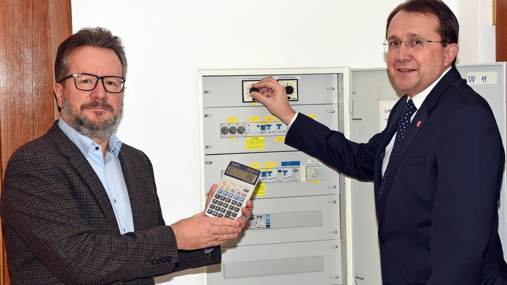 Thomas Zeh (Referatsleiter Technischer Umweltschutz) mit Taschenrechner und Bürgermeister Matthias Stadler stehen vor dem Stromzählerkasten. (Foto: Josef Vorlaufer)