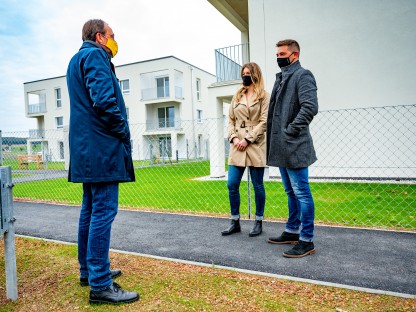 Ein Pärchen und Bürgermeister Matthias Stadler im Gespräch. Im Hintergrund ist der neu errichtete Wohnbau zu sehen, in dem Christopher Fertner und seine Freundin Lisa Wissijak einziehen werden. 
