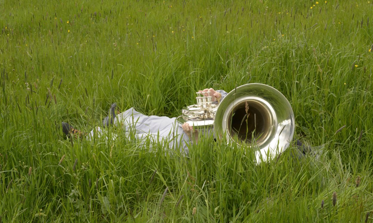 Shared Lanscapes führt zeigt die Verbindung von Mensch und Natur auf. Auf dem Bild ist jemand zu sehen, der im Gras liegt und dabei ein Blasinstrument spielt.