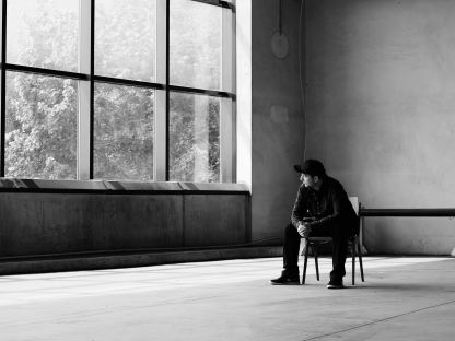 Schwarz-Weiß Foto des Musikers CHiLL-iLL. Er sitzt in einem großen Raum auf einem Stuhl und schaut durch eine große Fensterfront in die Natur hinaus. (Foto: Fabian Fallend)