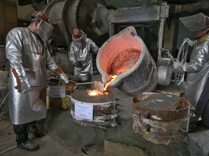 Drei Fachkräfte bei der arbeit: Sie gießen aus geschmolzenem Metall eine Glocke.