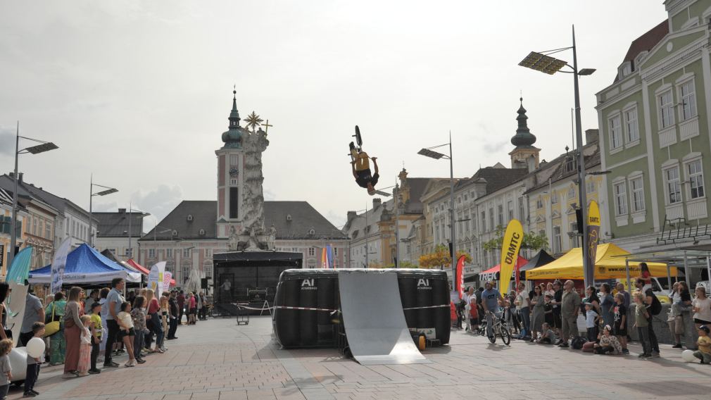 Ein Foto der BMX-Stunt-Show am Rathausplatz mit Publikum und den Infoständen der diversen Aussteller:innen. (Foto: Wolfgang Mayer)