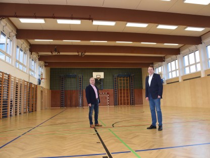 Bürgermeister Matthias Stadler und Schulamtsleiter Andreas Schmidt befinden sich im Turnsaal der MS Pottenbrunn, wo ein neuer Vollholzboden und neue Wandvertäfelungen verlegt wurden.