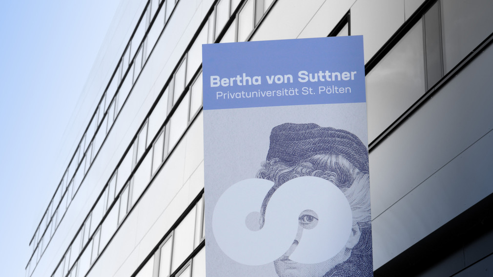 Im hintergrund erkennt man die Fassade der FH St. Pölten, davor ist ein Transparent, mit dem Logo der Bertha von Suttner Uni, angebracht.