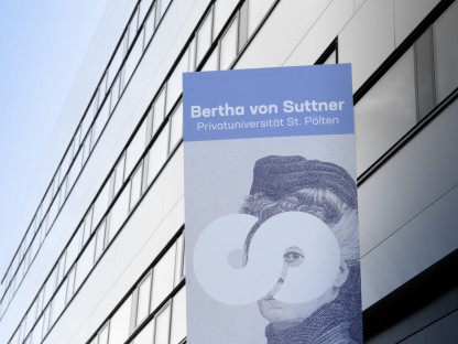 Im hintergrund erkennt man die Fassade der FH St. Pölten, davor ist ein Transparent, mit dem Logo der Bertha von Suttner Uni, angebracht.