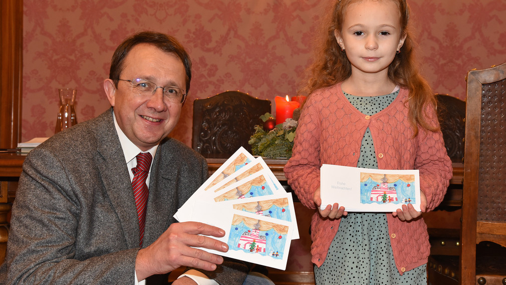 Bürgermeister Stadler und Emilia Schöne präsentieren die Weihnachtskarte mit Emilias Zeichnung.