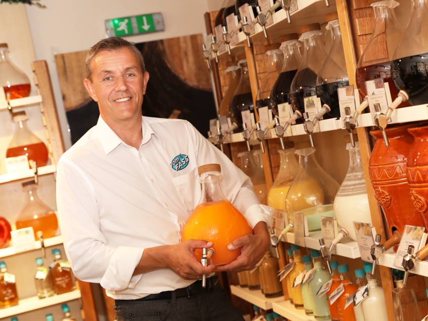 Gerhard Scholler steht zwischen den Regalen im Feinkost-Laden vomFASS St. Pölten und hält eine Flasche in der Hand. Foto: kommunikationsagentur-sengstschmid